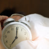 A sleeping person reaches for his alarm clock