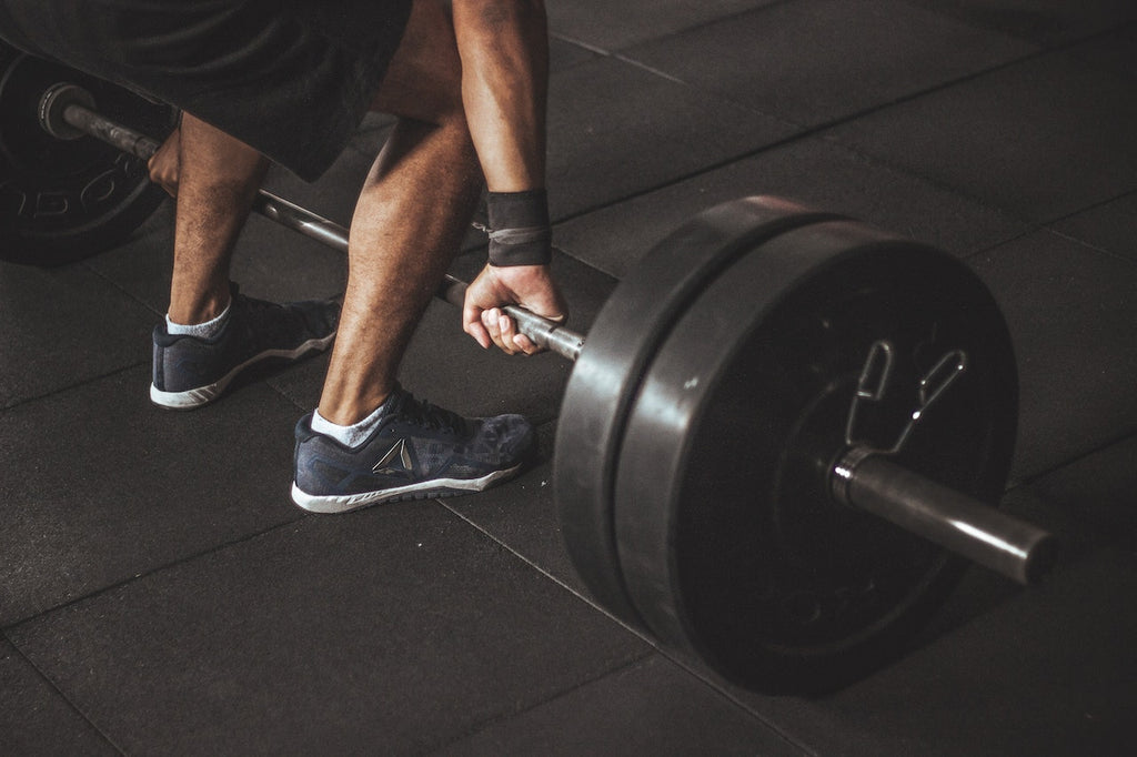 Man wearing shoes with arms out about to lift a bar of heavyweights at the gym