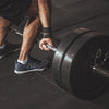 Man wearing shoes with arms out about to lift a bar of heavyweights at the gym